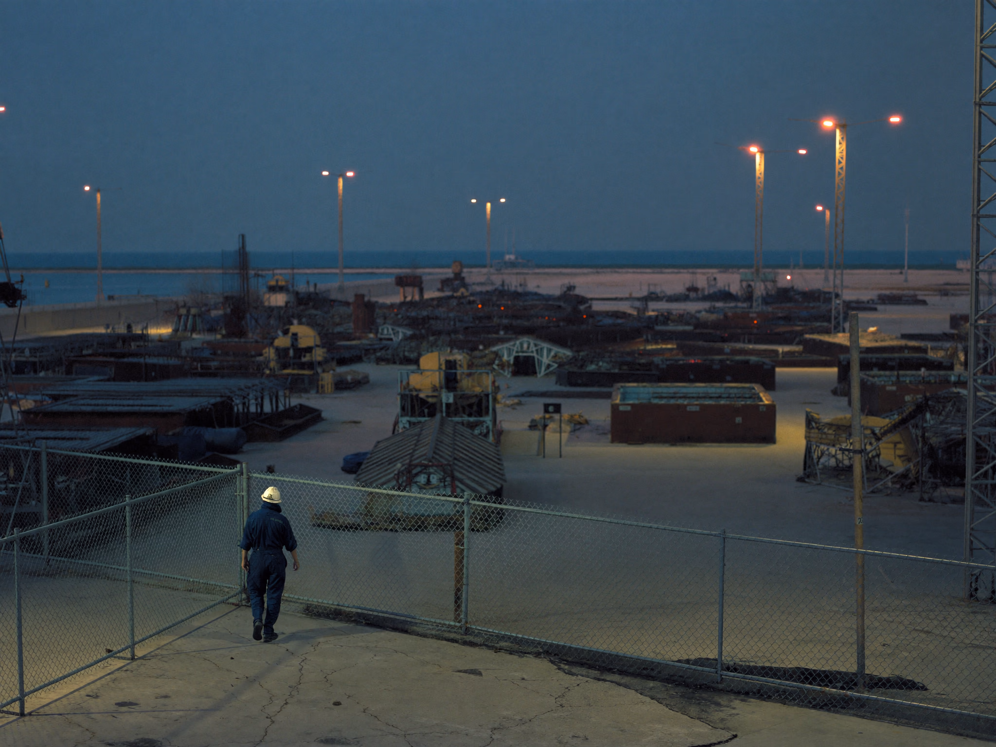 Worker walking toward a lit industrial yard at twilight