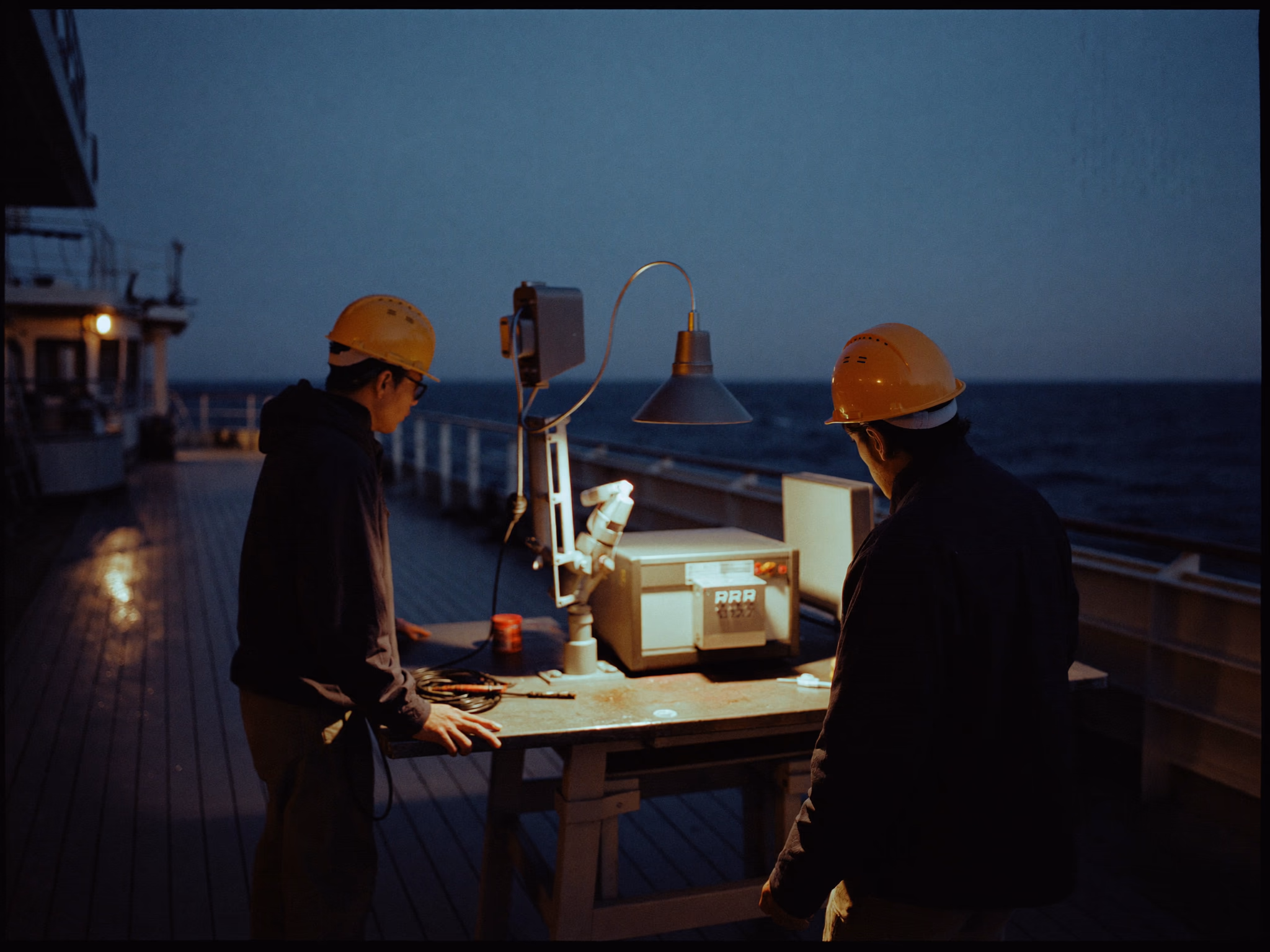 Two workers inspecting technical equipment on a ship deck at night